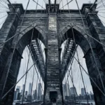 Graphite brooklyn bridge wall art print featuring granite archways, steel cables, architectural details, and dramatic urban perspective for elegant interiors