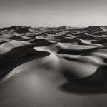 Charcoal and gold black and white photo artwork print featuring flowing sand dunes with sculpted ridgelines, shadows, and luminous highlights